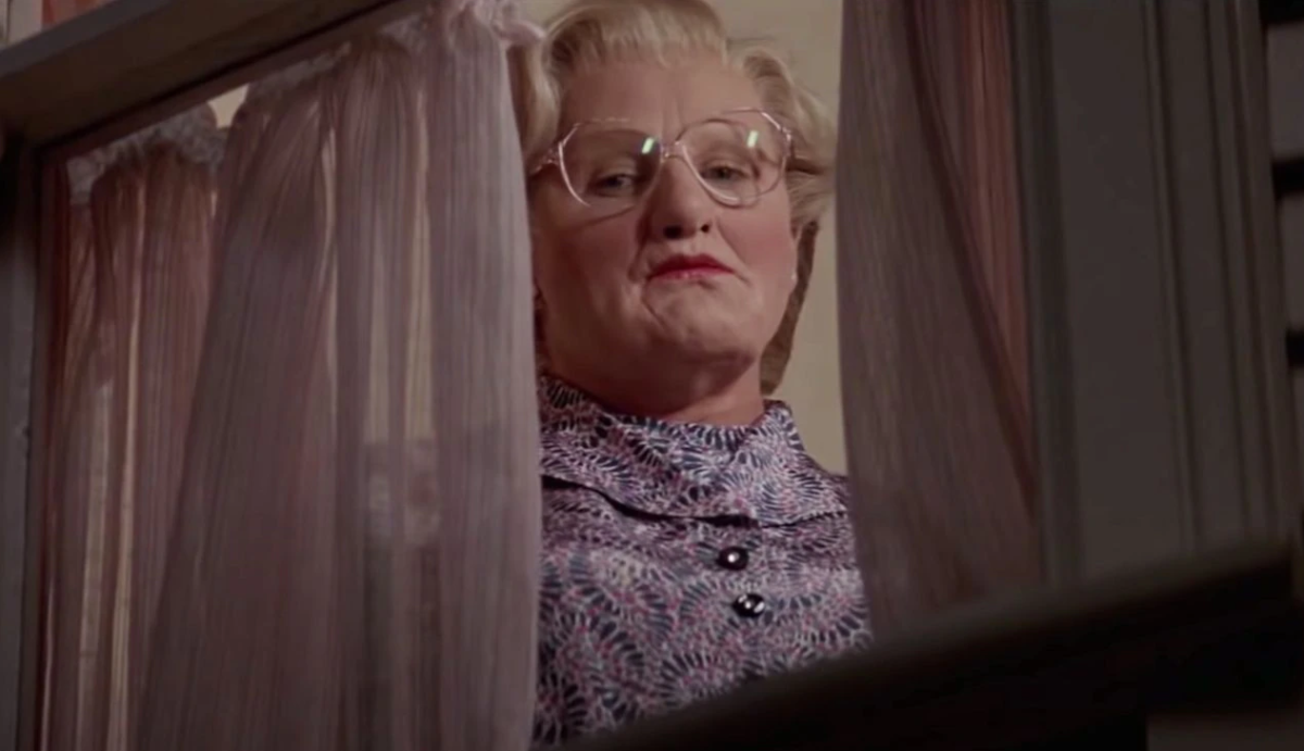 Robin Williams dressed as Mrs Doubtfire looking angrily out of an upstairs window