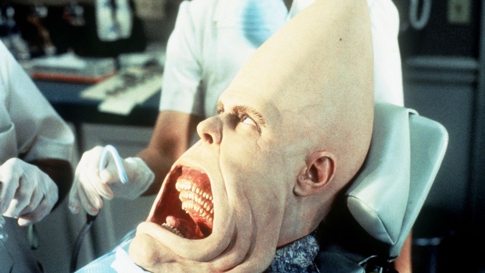 Beldar Conehead sitting in a dentist chair with his mouth gaping open in an alien horrid way